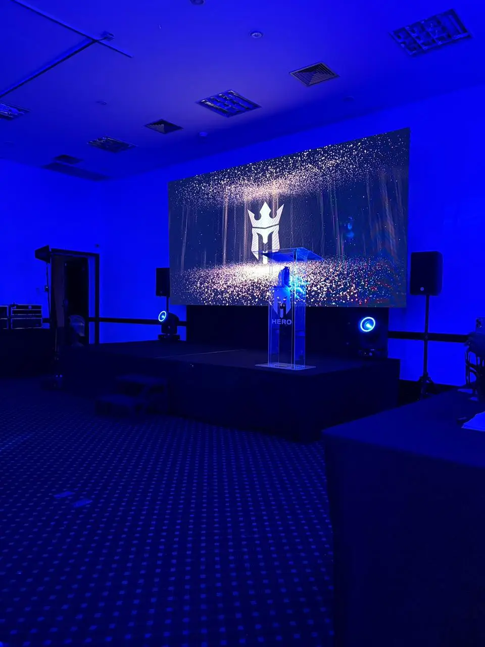 Palco montado em auditório de hotel, com painel de LED ocupando todo o fundo, púlpito de acrílico e caixas de som nas duas pontas.